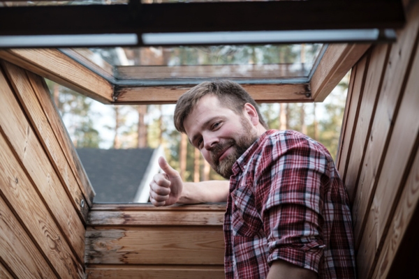 Bearded man by an open attic roof window after air leak inspection
