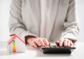 cropped view of a woman with a calculator and a miniature house depicting energy efficiency and savings