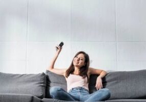 woman on the couch turning on home AC with a remote during summer