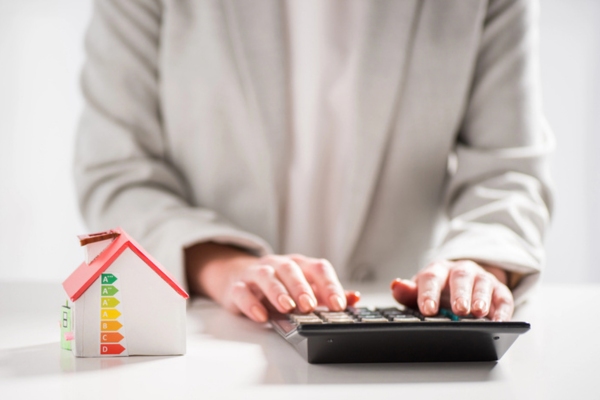 cropped view of a woman with a calculator and a miniature house depicting energy efficiency and savings