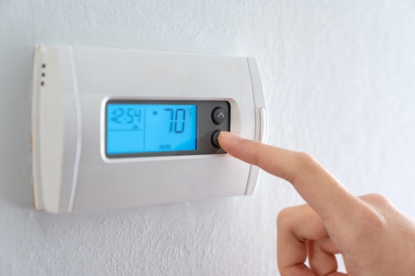 homeowner turning thermostat down to keep cool in the summer