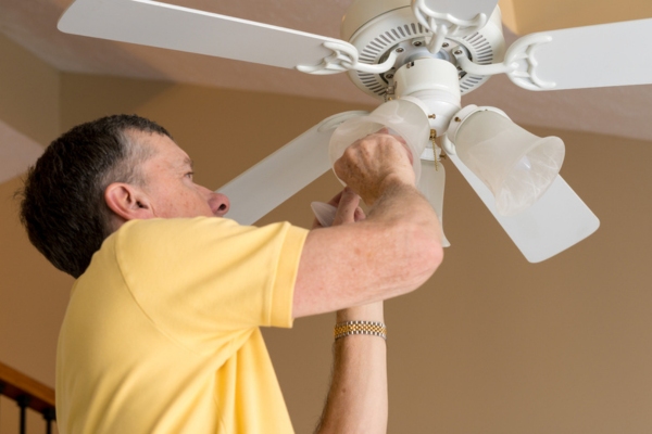 man cleaning ceiling fan and changing light bulbs